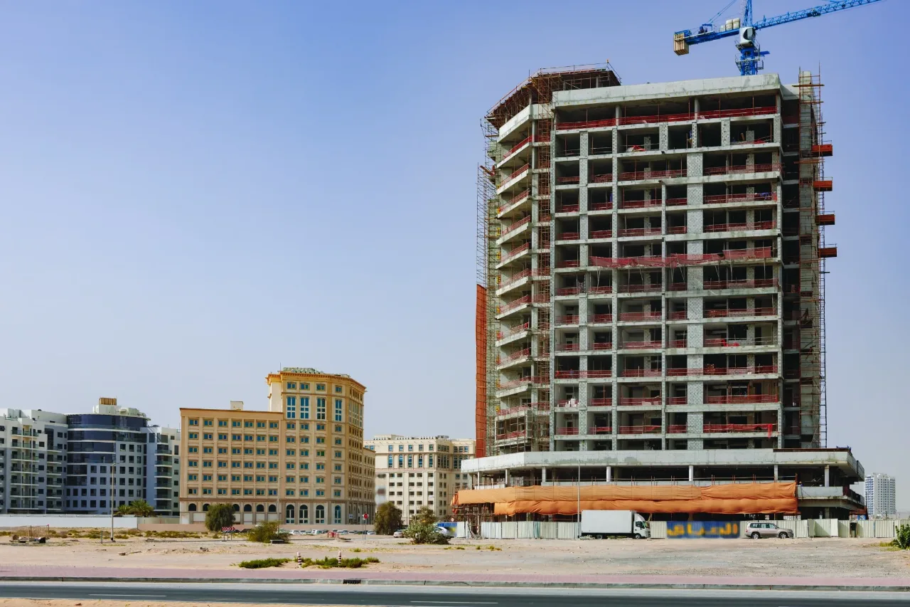 A mid-rise building under construction beside completed low-rise buildings on a street edge