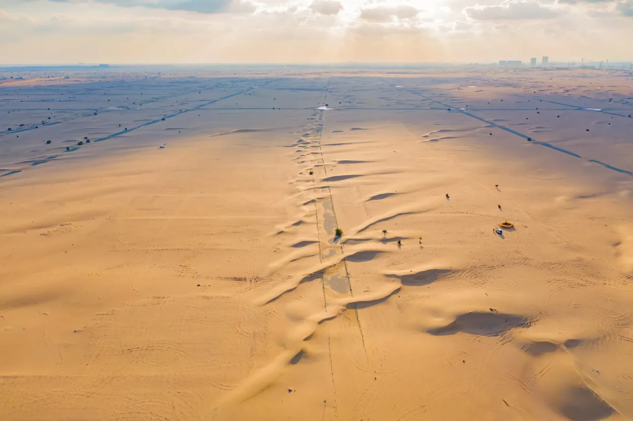 Aerial view of open desert with a sand-covered road and survey lines running to a distant town