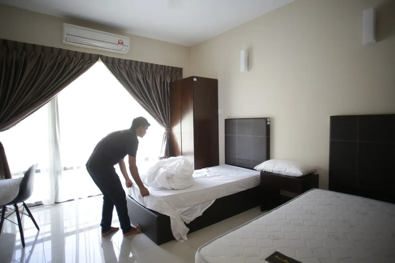 A resident makes up a bed in a bright twin room with fitted wardrobe and air conditioning