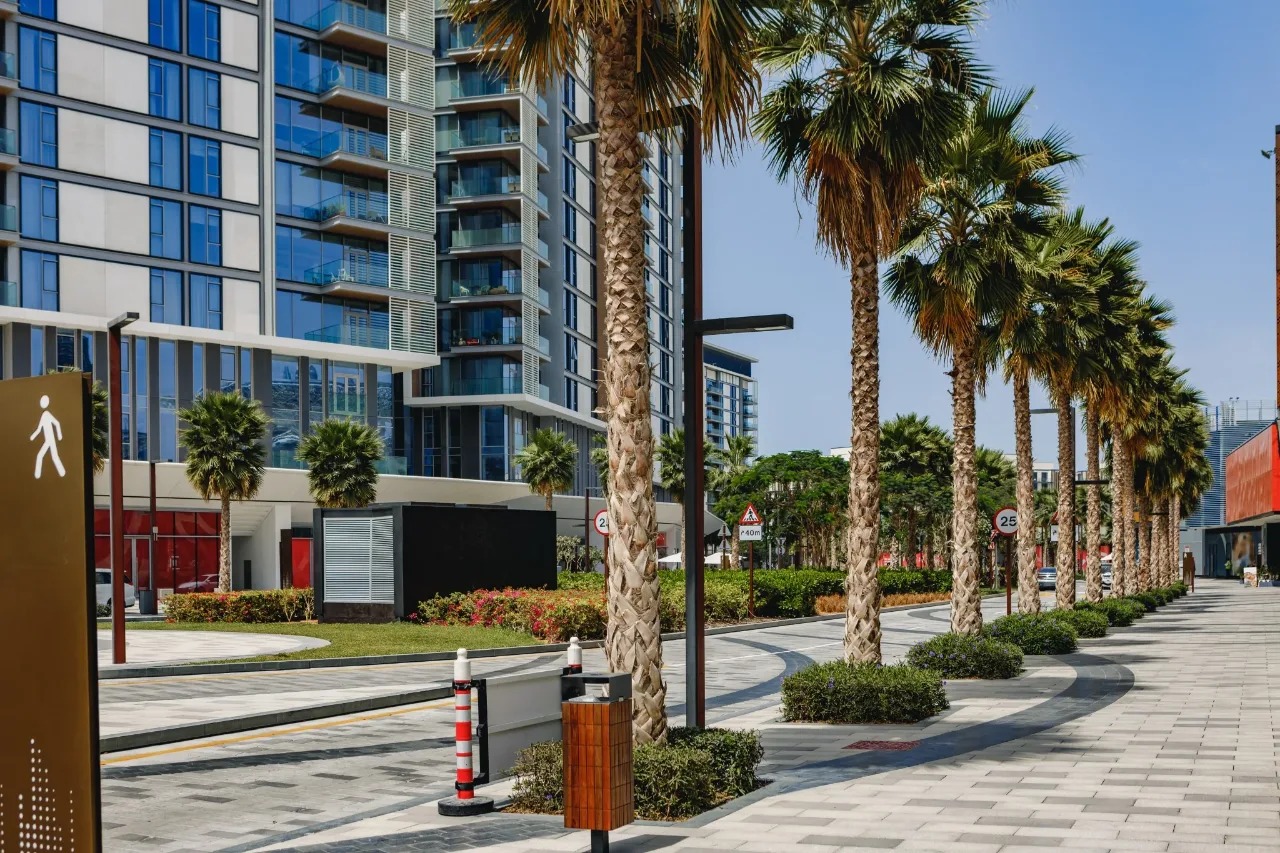 A shaded, palm-lined walkway with lighting, seating and signage between residential buildings and shared amenities